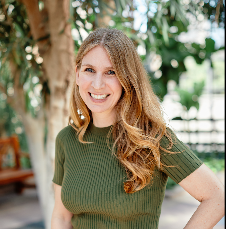 Shelby smiles in a greenhouse. She has long, blond hair and wears green.