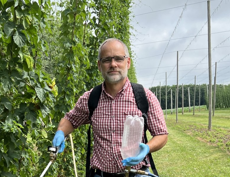 Dan smiles slightly and holds a pesticide applicator.