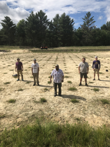 Five people stand in a field in a "V" shape.