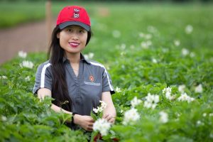 Yi Wang smiles brightly. Yi is in a field with bright white blossoms.
