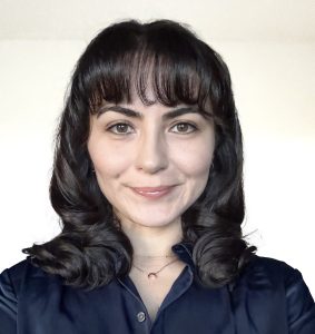 Gunay smiles. Gunay has black hair and wears a black blouse.