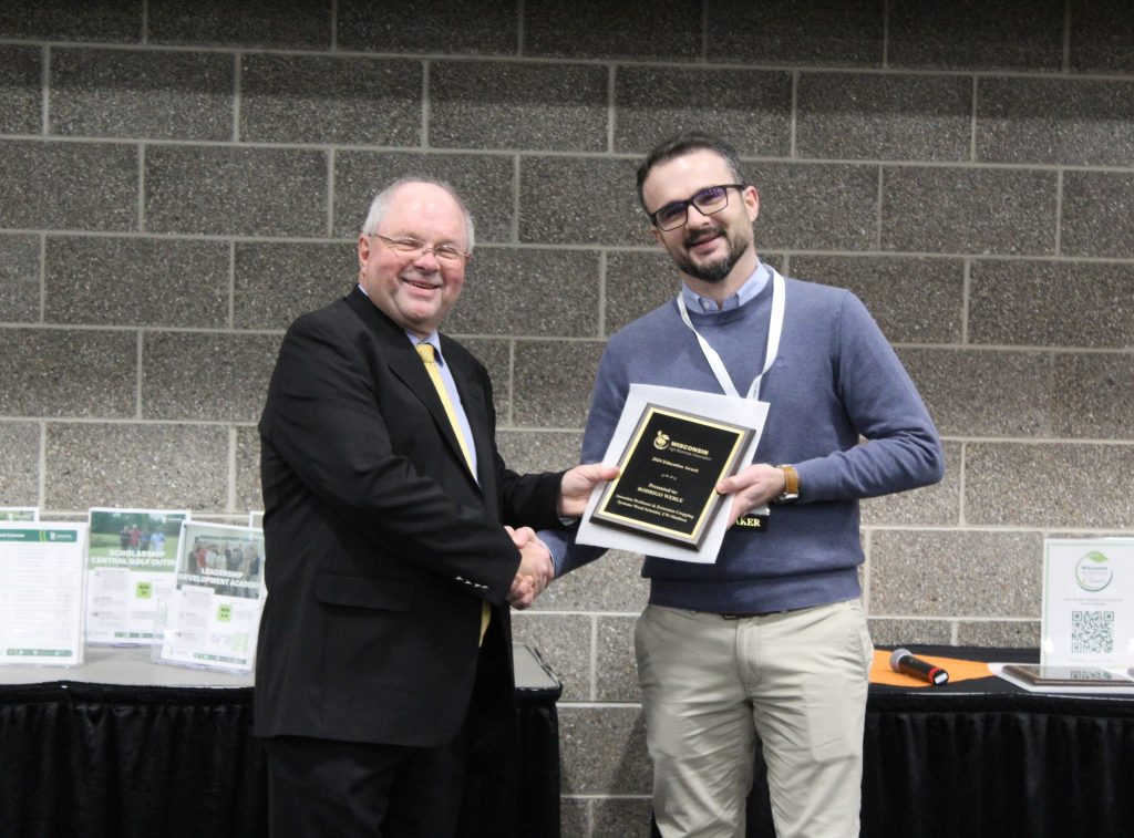 Tom Bressner wears a suit and shakes hands with Rodrigo Werle while passing an award.