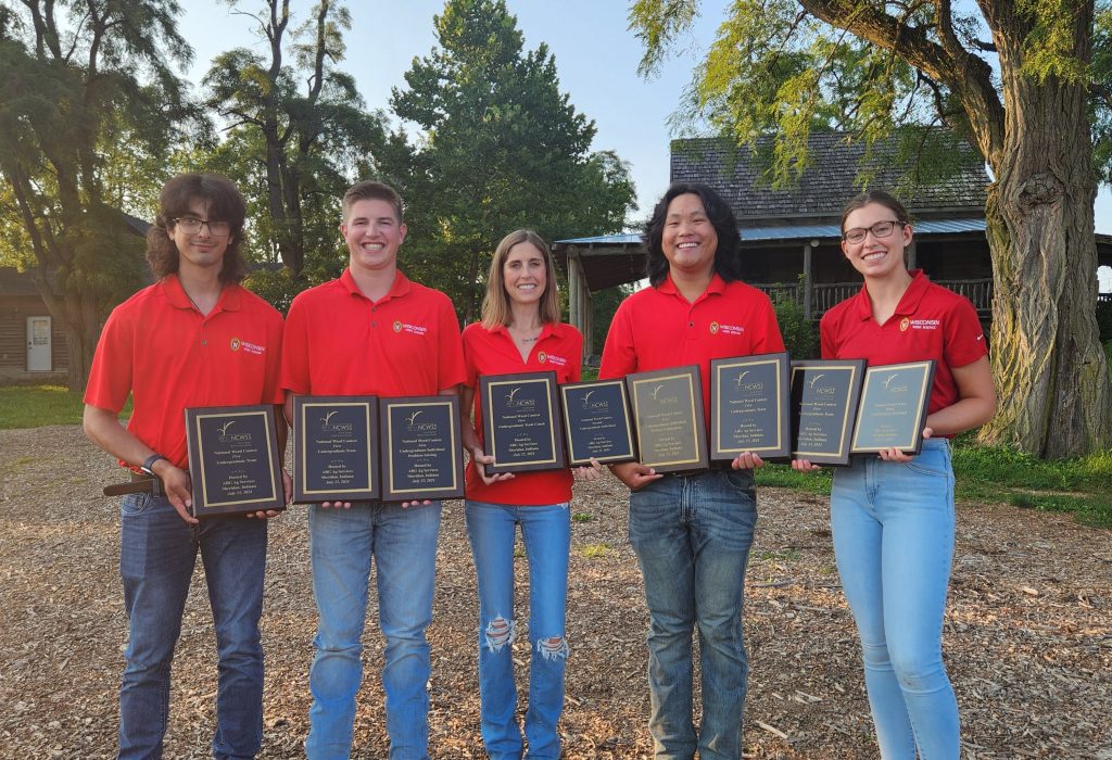 Five people wearing bright red polos and holding awards pose and smile.