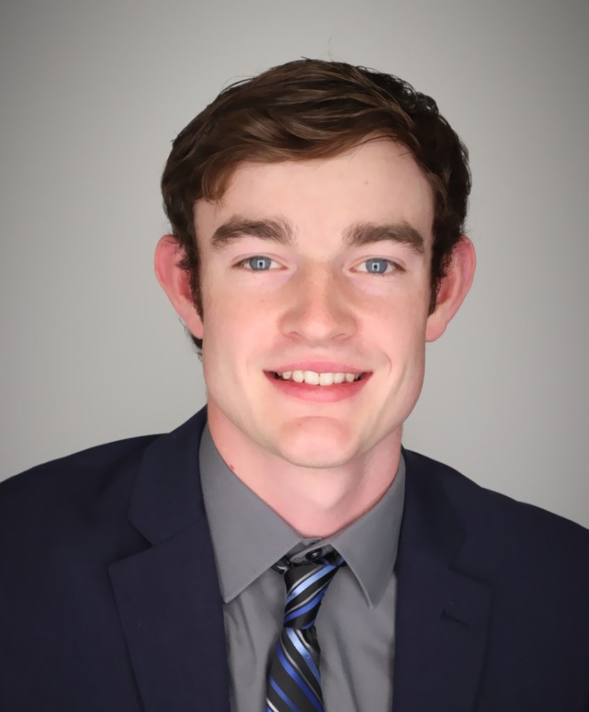 Lawson poses for a professional headshot. Lawson is wearing a suit, grey button up, and tie.
