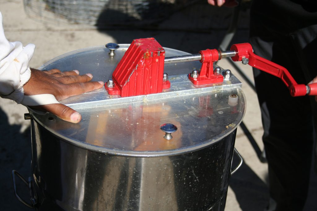 A person holds down a large metal container that has a hand crank.