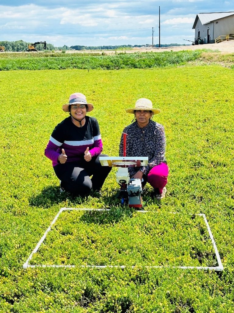 Dharani Suresh Babu and Jyostna Devi Mura sit in a field and monitor a Raspberry Pi camera.