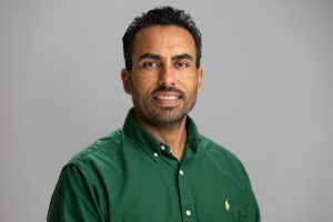 Raj smiles. He has short, black hair and wears a forest green button up.