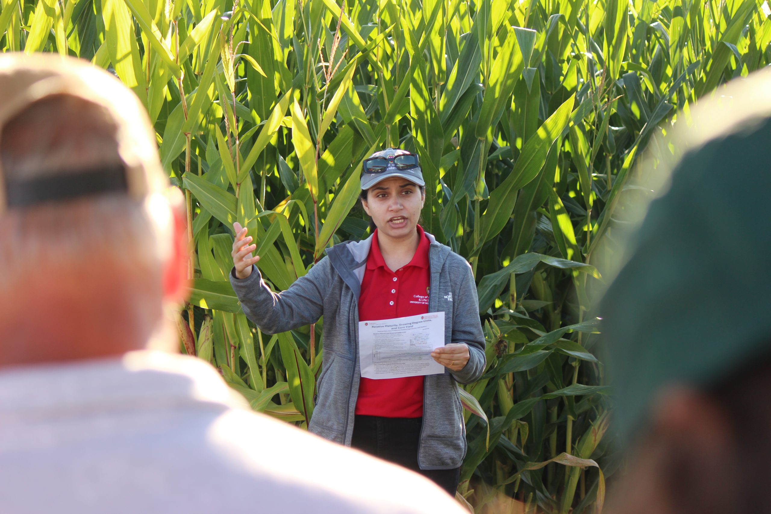 A person speaks to a crowd in front of corn.