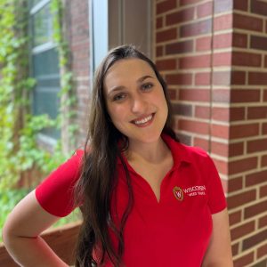 Alice smiles. She wears a bright red polo.