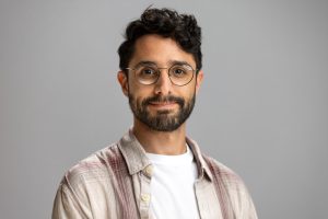 Luis smiles. He has curly, black hair and oval glasses.