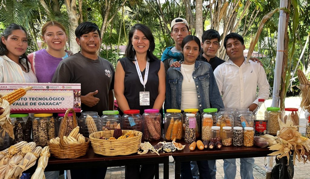 A group of students and Calderon present at a table of native maize varieties.