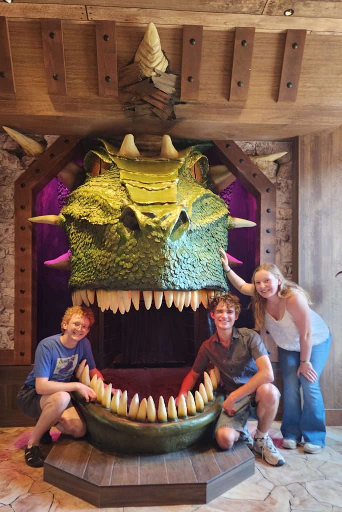 Three students pose next to an artistic, sculpted dragon head.