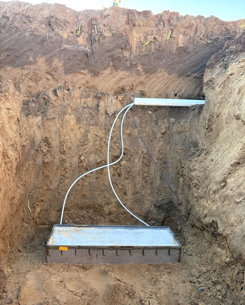 A large, metal lysimeter is buried deep within the ground.