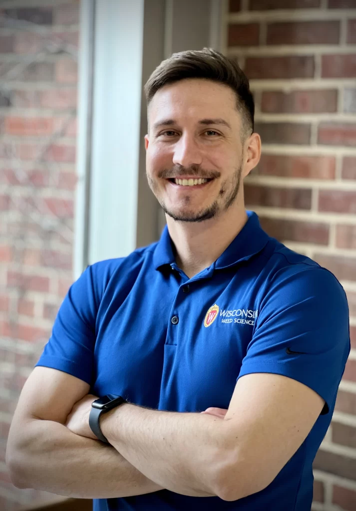 Nikola smiles for a professional portrait. He wears a cobalt blue polo with a UW logo on it.