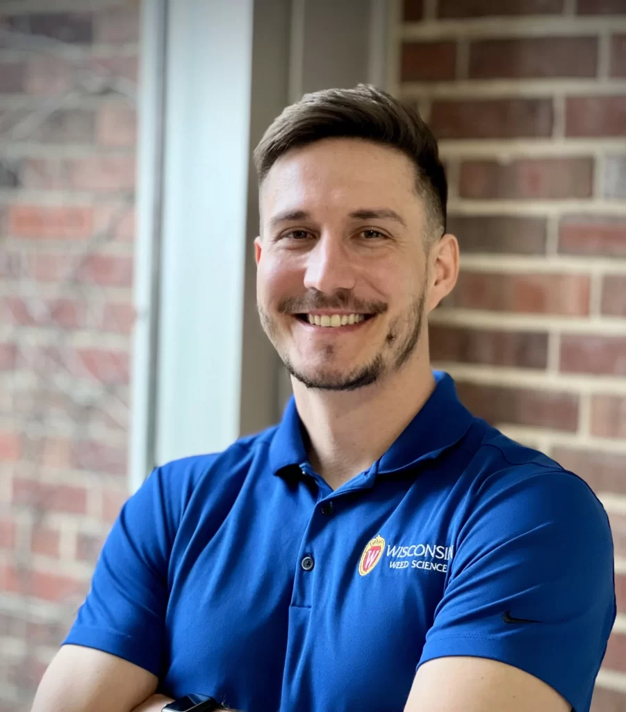 Nikola smiles for a professional portrait. He wears a cobalt blue polo with a UW logo on it.