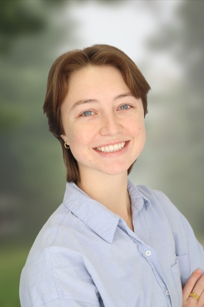 Breawna smiles for a professional photo. Breawna has short, brown hair and wears a blue button up.