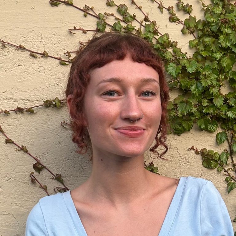 Aubrey smiles. Aubrey has curly hair and short bangs and wears a blue shirt.