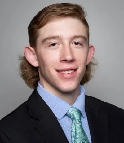 Bryce smiles for a professional portrait. Bryce wears a suit and has auburn hair.