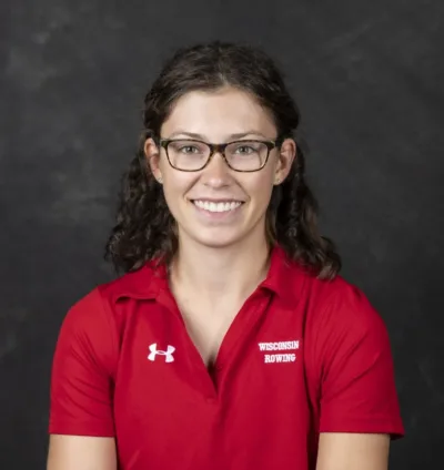 Rianne smiles for a professional portrait. Rianne has long, dark hair and wears a red polo.