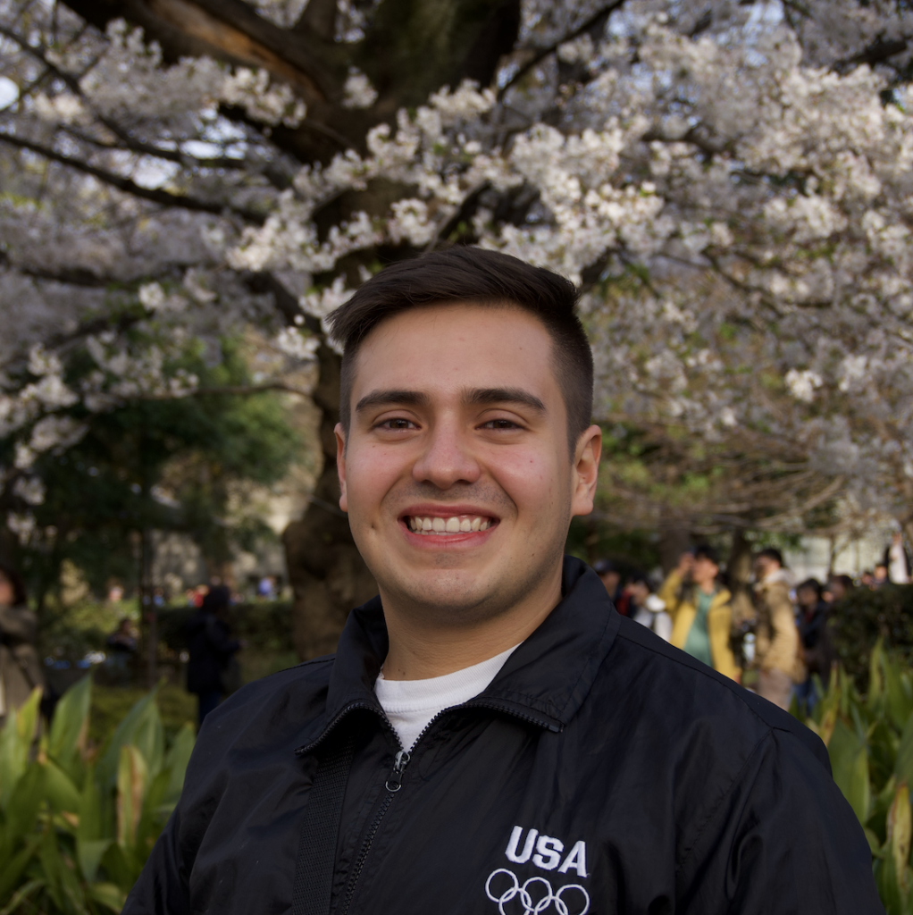 Sven smiles and wears a USA Olympics polo. In the background, a tree blossoms.