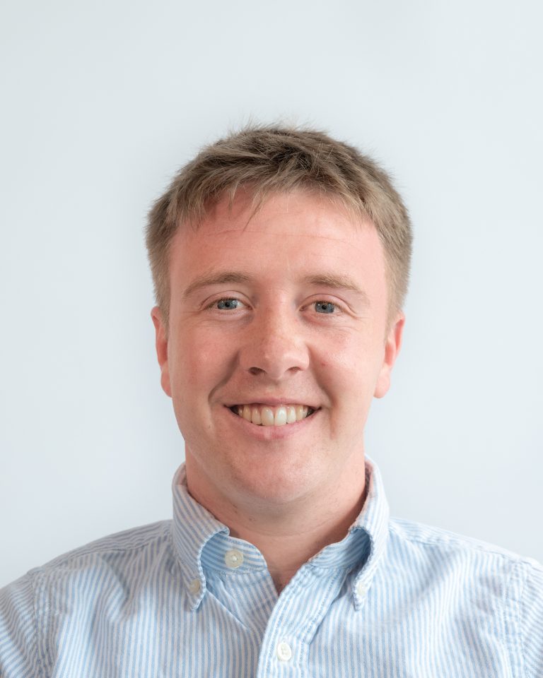 Tomas smiles for a professional portrait. He wears a blue button up and has short hair.